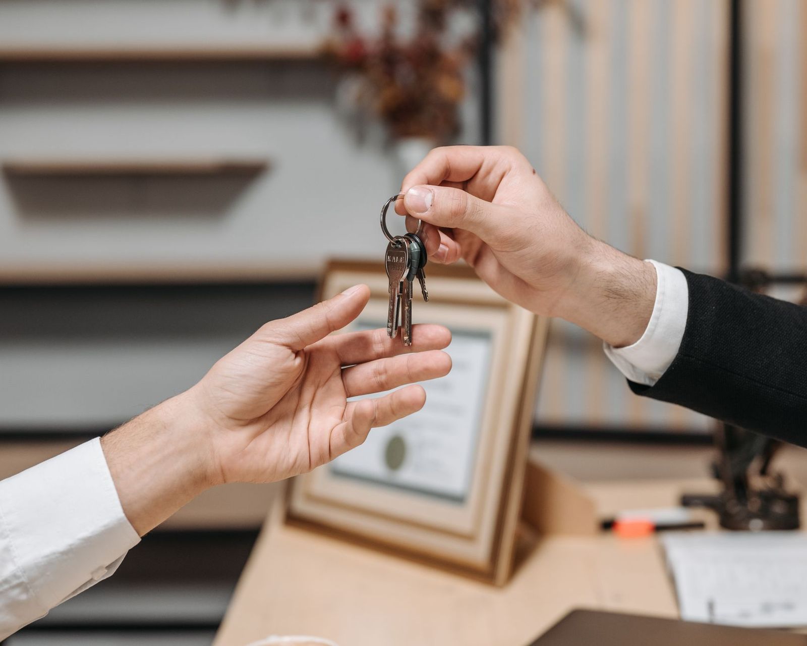 Outgoing business owner handing a set of premises keys across a desk to the buyer after the lease is assigned