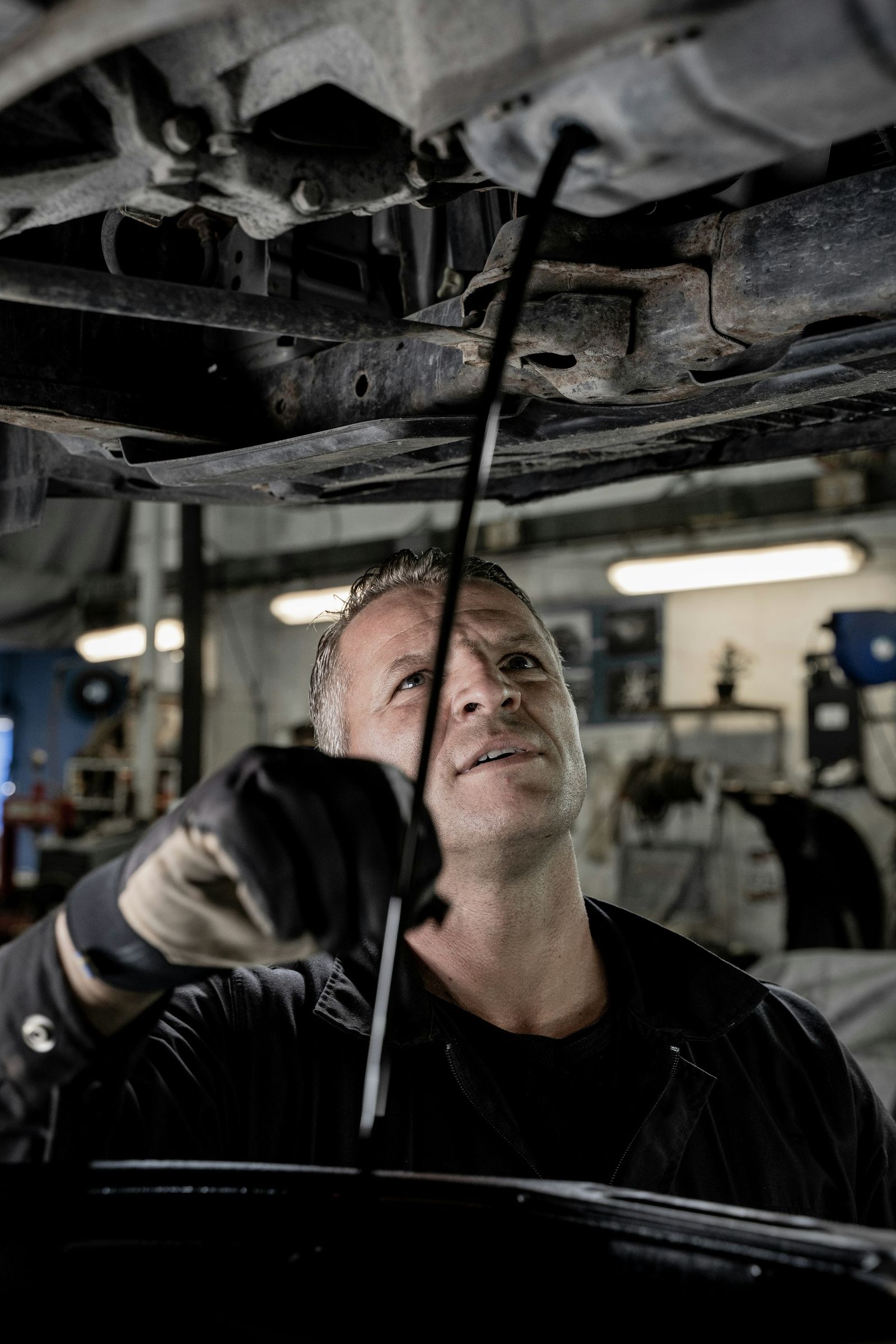 Mechanic in protective gloves servicing a car in a busy workshop