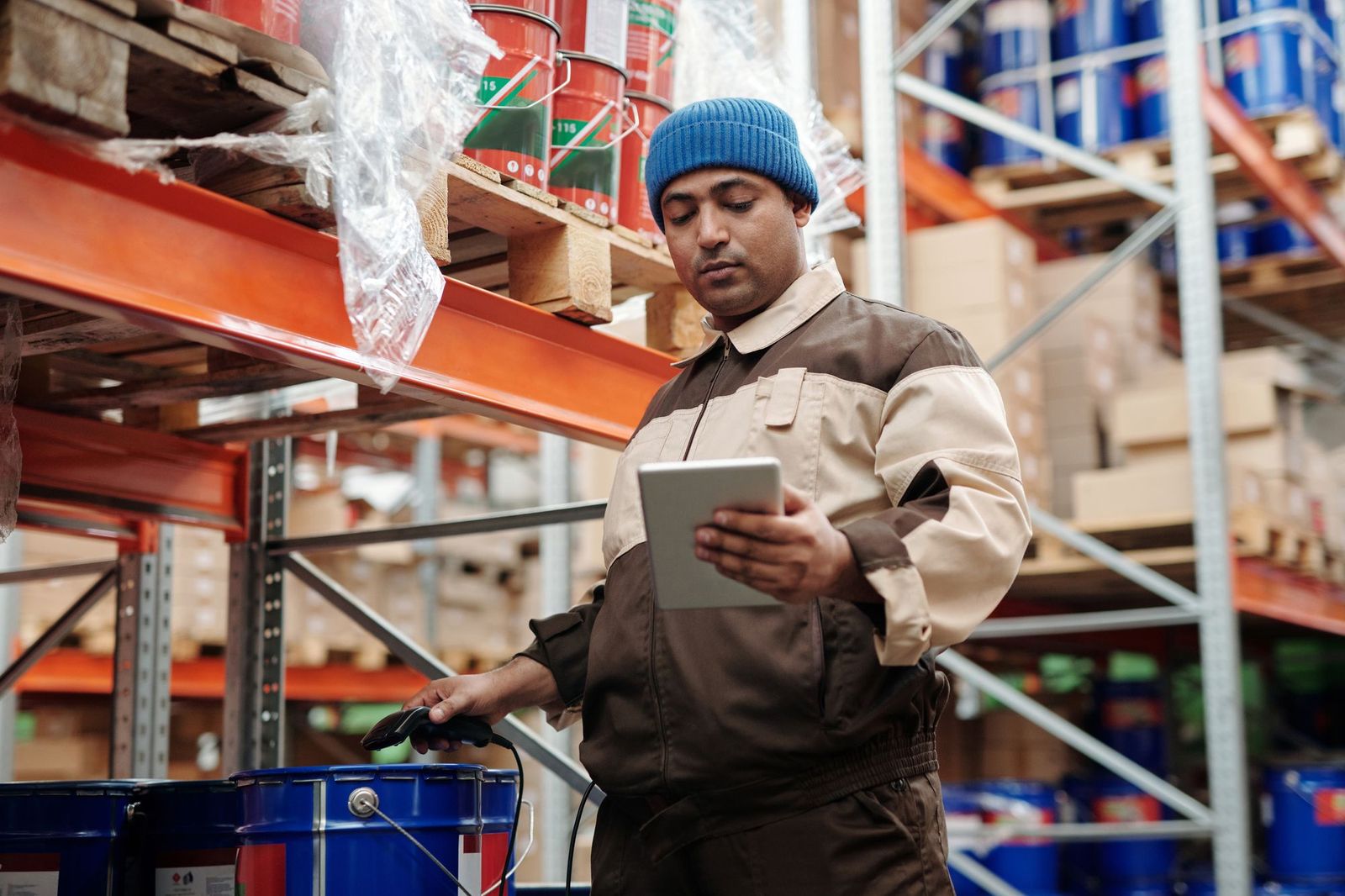 Warehouse manager in a work jacket counting stock on a tablet beside pallet racking stocked with paint tins